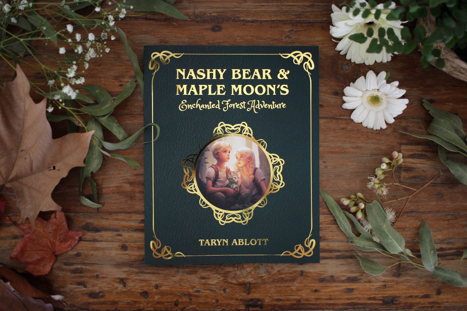 A copy of Nashy Bear and Maple Moon's Enchanted Forest Adventure laid upon a wooden table and surrounded by leaves and flowers.